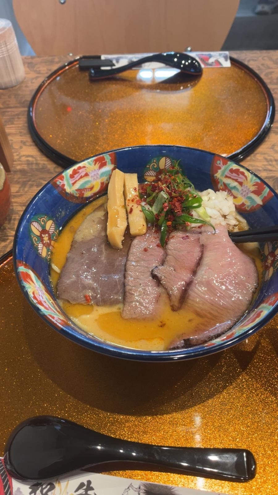 Un bol de ramen au bœuf, aux tranches de viande et à la ciboulette, dans un bol bleu décoré